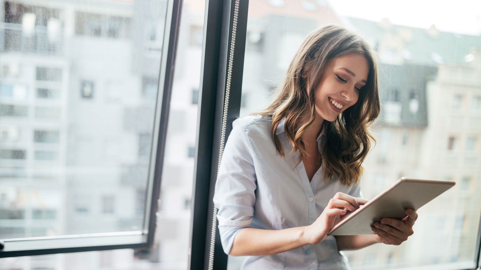 Woman leaning on a window typing on a tablet